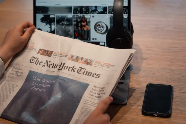 Close-up of hands holding a newspaper by a laptop and smartphone on a table. Räckvidd och kostnadsmått: traditionella/digitala kanaler