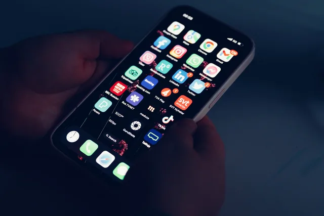 Close-up of hands holding a smartphone displaying various app icons in a dimly lit room. Kostnadsdrivare i svenska mediekanaler: en checklista för budgetunderlag